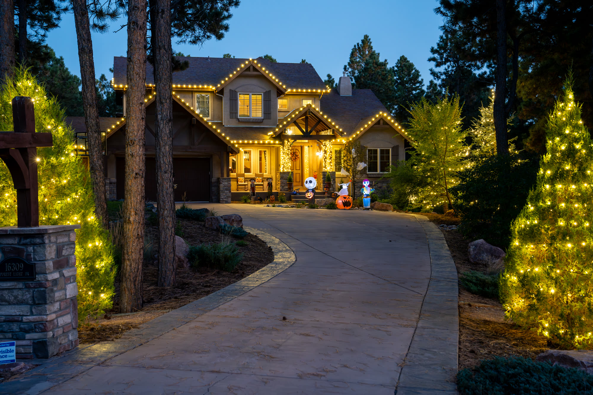 Home with warm white C9 Christmas string lights on the roofline and trees along the driveway